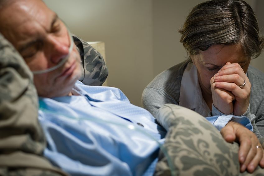 Old wife praying for terminally ill husband lying in coma