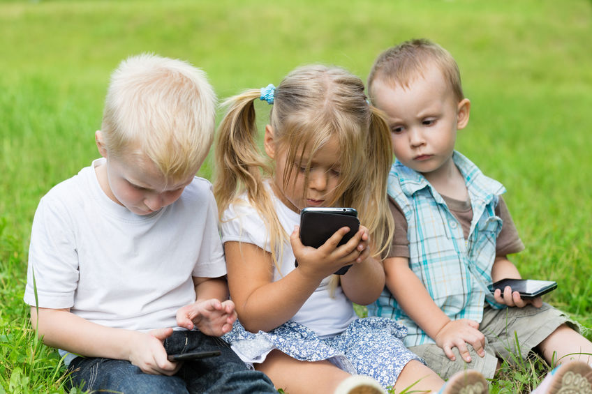 Kids playing on smartphones sitting on the grass in the park.